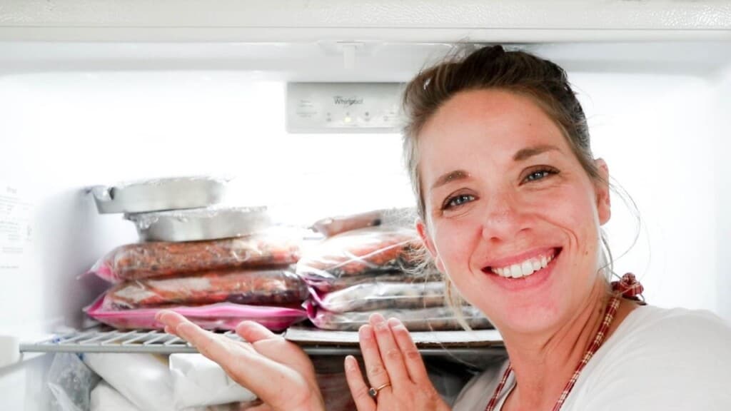 women smiling and pointing to freezer meals stacked in her freezer