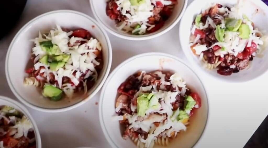four white bowls full of chili and topped with avocado and cheese