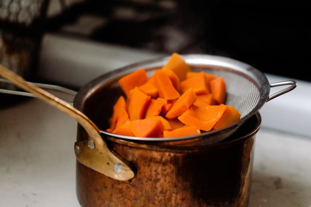 chopped pumpkin in a fine mesh strainer over a copper pot