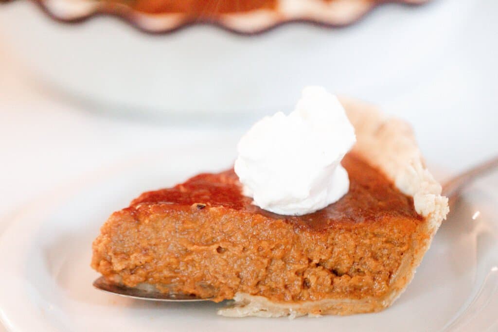 slice of pumpkin pie being served with a cake knife on a white plate