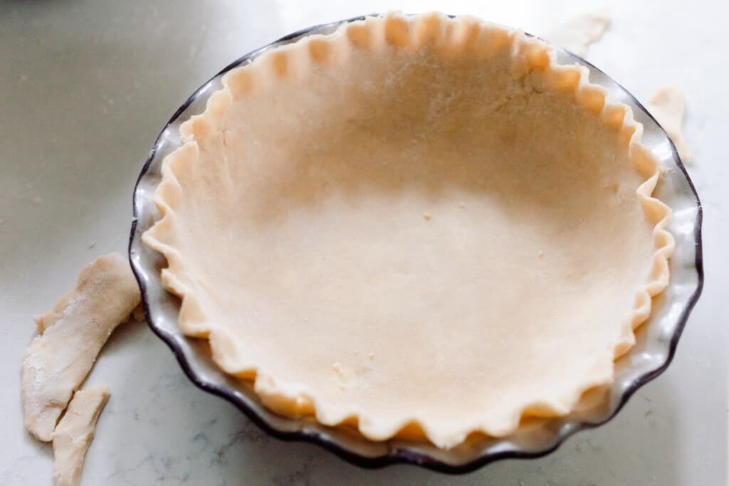 pie dough rolled out in a pie dish with the edges trimmed and chipped