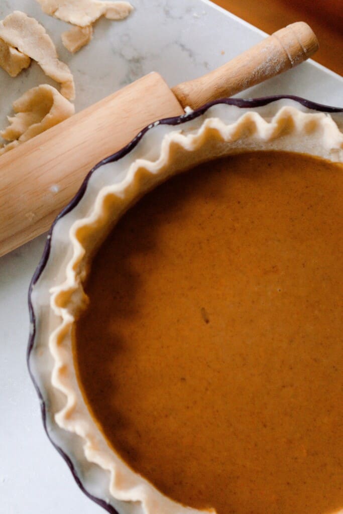 unbaked pumpkin pie on a quarts countertop with a rolling pin in the background