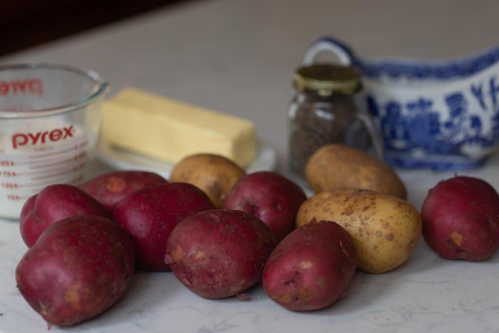 red and russet potatoes with butter, cream, on a white countertop. Little containers of salt and pepper in the background.