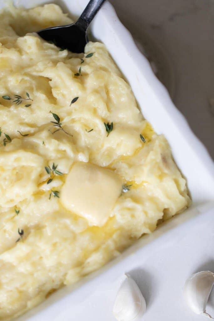 overhead photo of garlic mashed potatoes with herbs sprinkled on top with a pat of butter.
