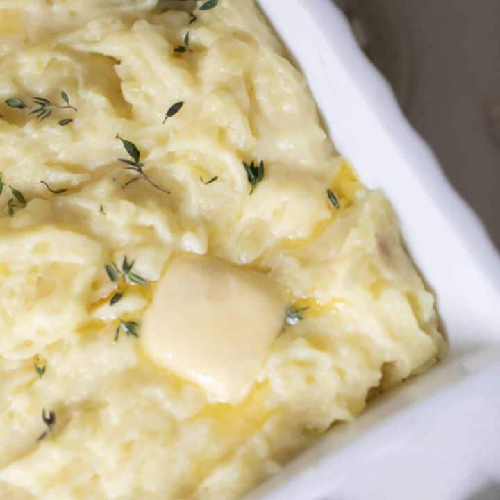 overhead photo of garlic mashed potatoes with herbs sprinkled on top with a pat of butter.
