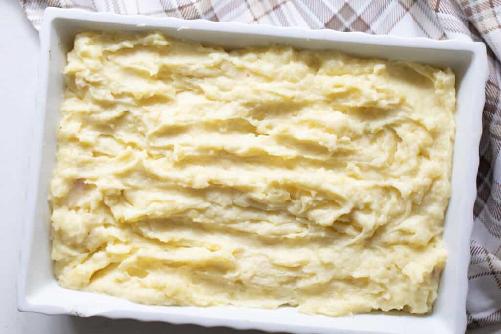 baking dish full of garlic mashed potatoes resting on a tan and cream towel