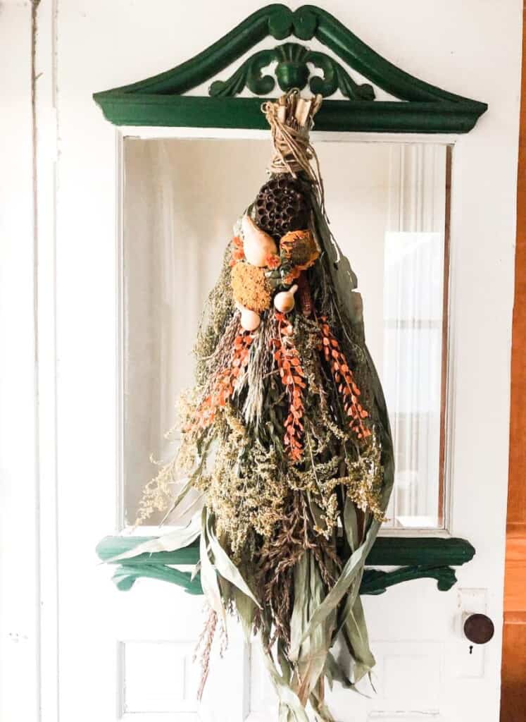 Dried florals in a bunch hanging upside down on a green and white door with glass