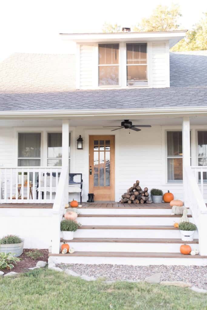 fall farmhouse front porch with pumpkins up the stairway and wood stacked next to the door.