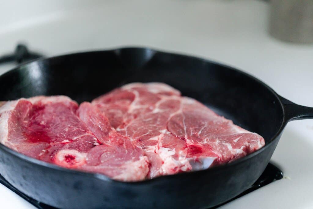 raw pork steaks browning in a cast iron skillet