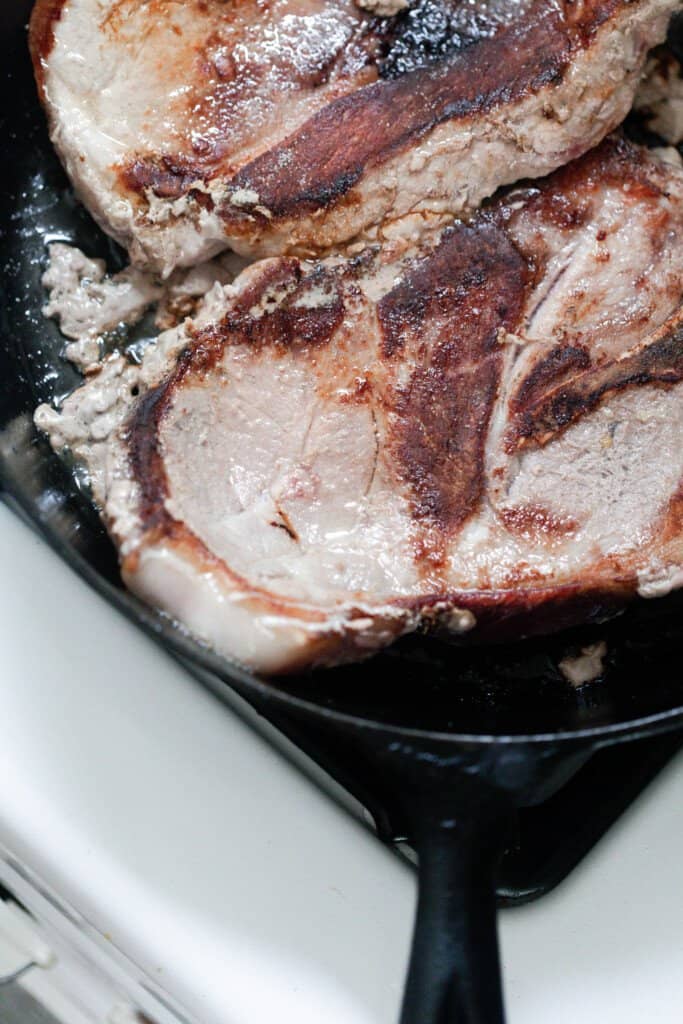 pork steaks browning in a cast iron skillet