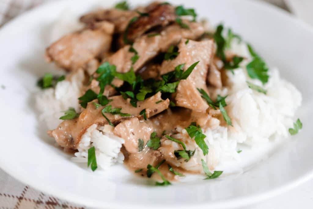 white plate with white rice, pork steak sliced and covered in a cream sauce