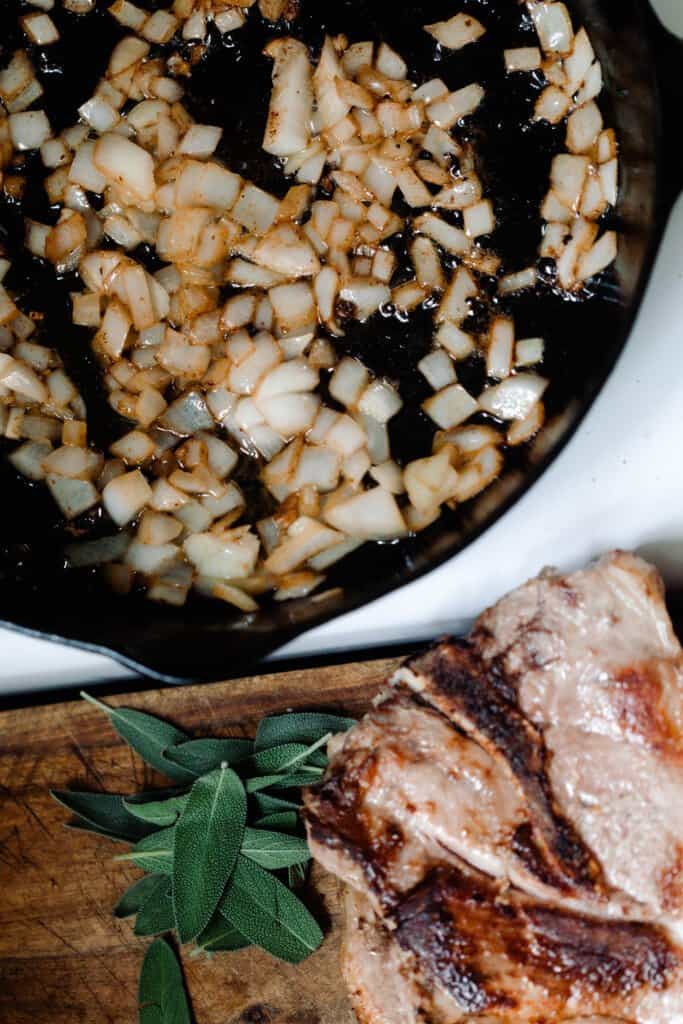 onions caramelized in a cast iron skillet on a stove. A cutting board with pork steaks and parsley