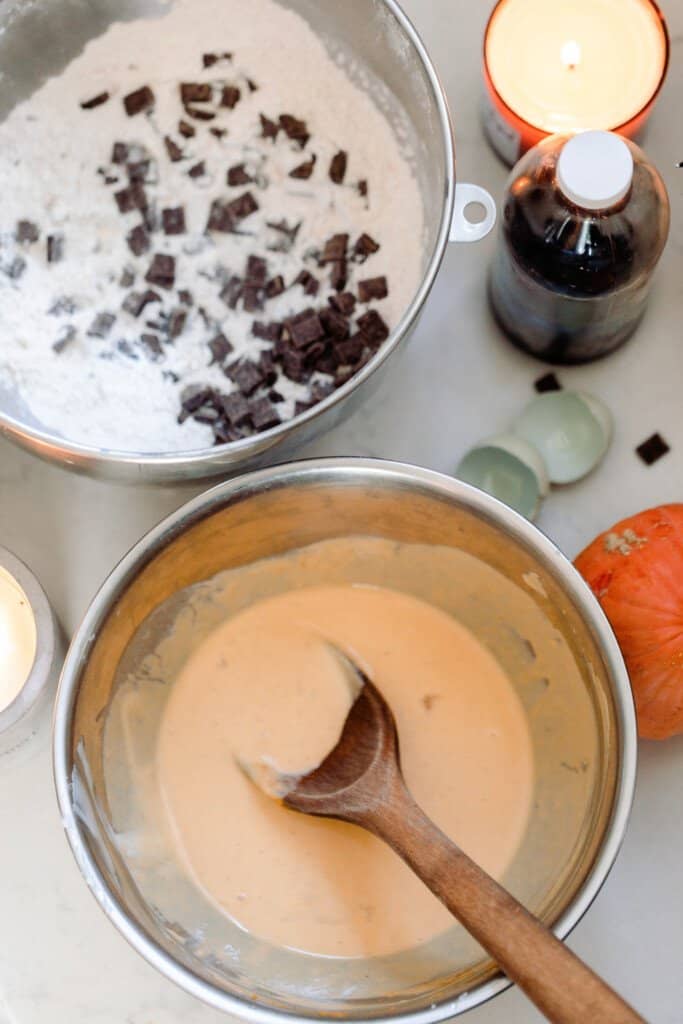 two bowls on a white quartz countertop. One bowl is dry ingredients and chocolate chips while the other has the wet ingredients for pumpkin scones