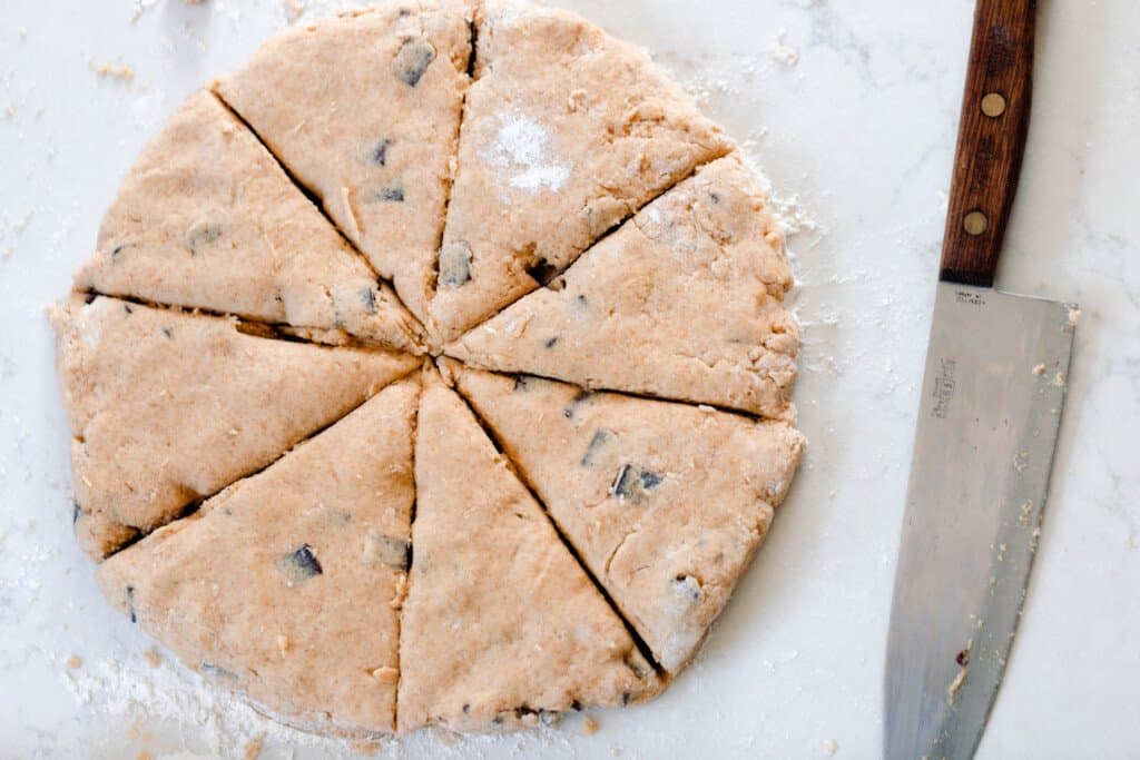 overhead photo of sourdough chocolate chip pumpkin scones in a circle and cut into 8 equal pieces on a white countertop with a chef knife to the right 