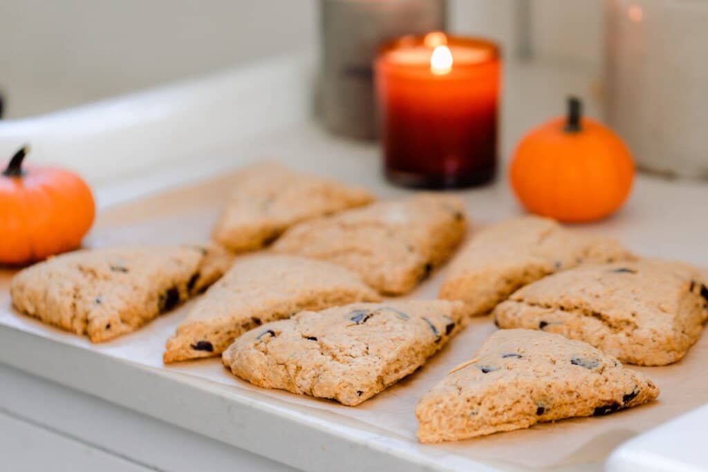 sourdough pumpkin scones cooling on a parchment lined baking sheet with small pumpkins and a candle in the background