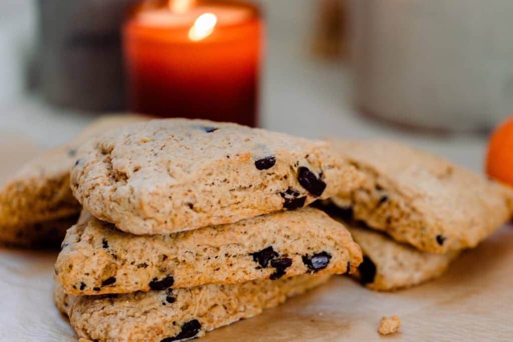 sourdough pumpkin scones with chocolate chips stacked 3 high with more scones in the background and an orange candle