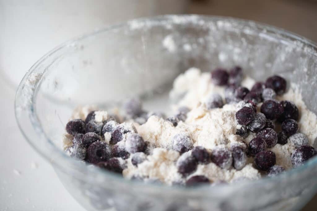 blueberries added to a flour, butter, and sugar mixture in a glass bowl