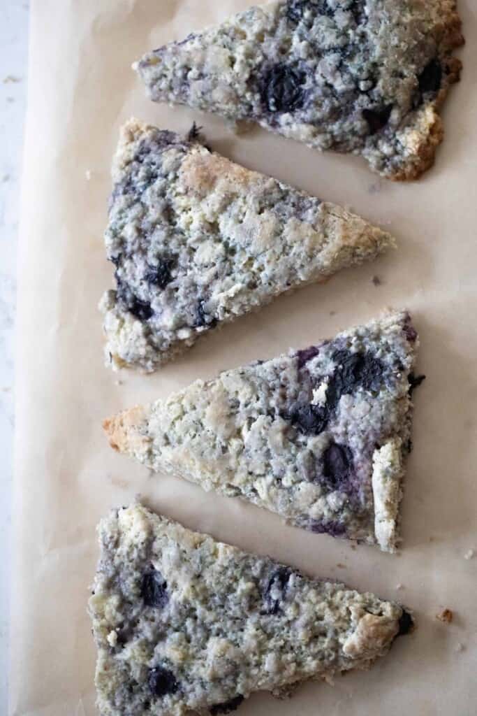 four sourdough scones with blueberries lined up on parchment paper