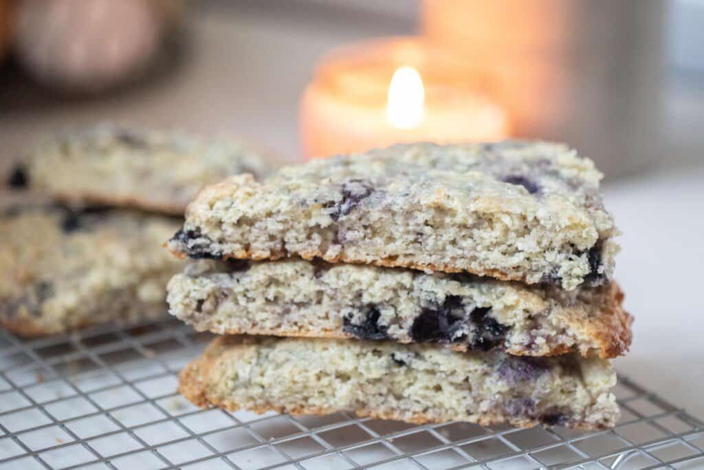 three sourdough scones with blueberries stacked up on a wire rack on a white countertop