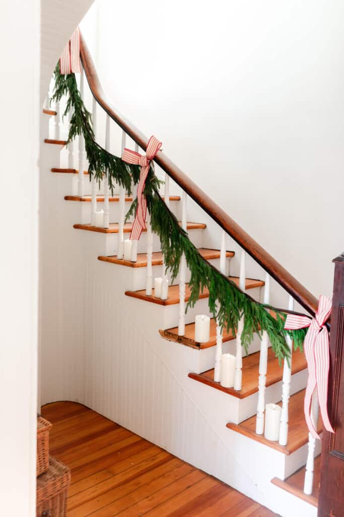 garland hand from a old farmhouse stair railing with red and white ticking stripe ribbon. Faux candles line the steps