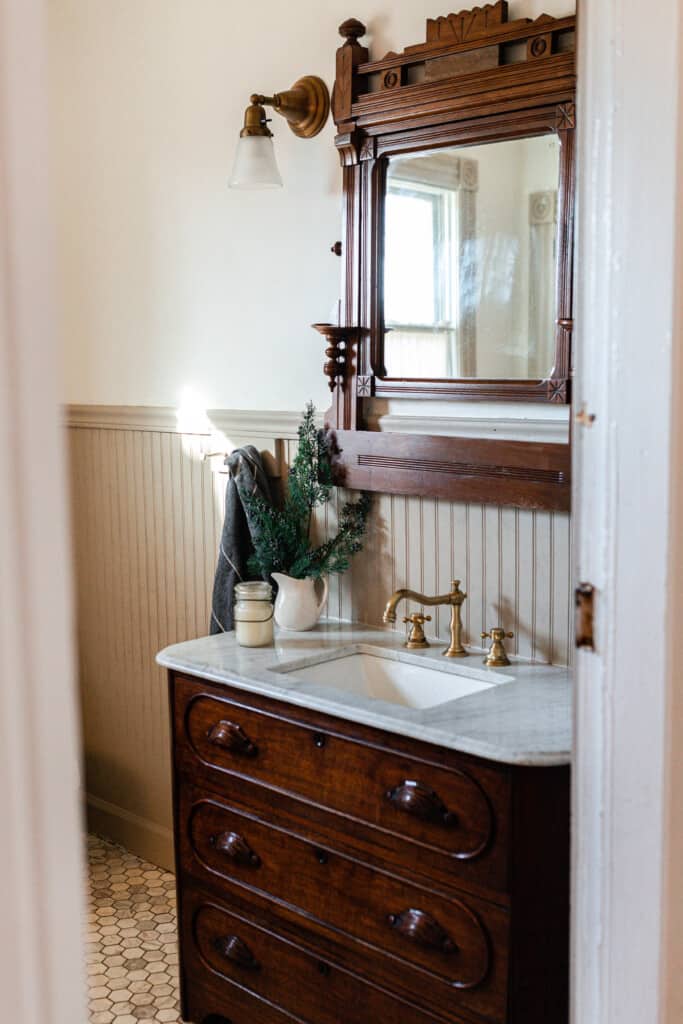 marble antique vanity with a vintage mirror hanging above. A ironstone pitcher is decorated with cypress branches sitting on the vanity top.