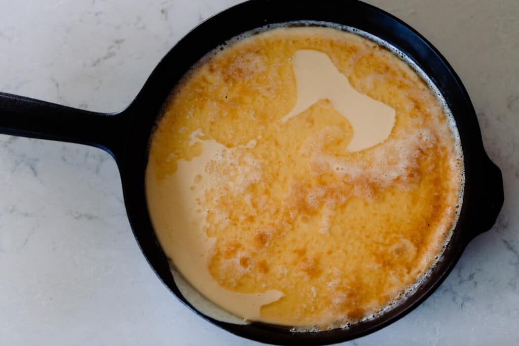 sourdough dutch baby pancake batter poured into a cast irons skillet with butter