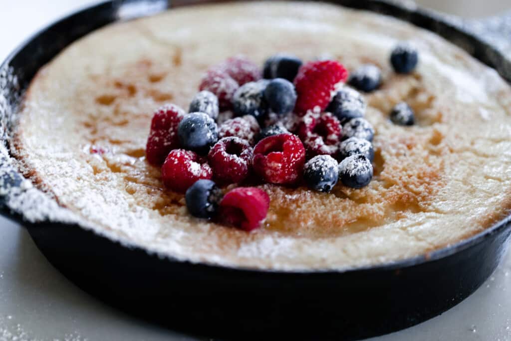 side view of a cast iron skillet pancake topped with berries and powdered sugar