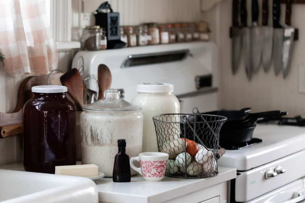 Flour, eggs, vanilla, sourdough starter and milk on a white countertop next to a white antique stove