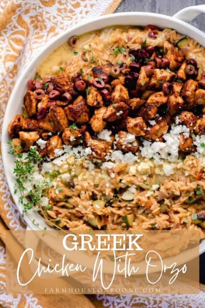overhead photo of Greek chicken with orzo pasta, feta, and retables in a white enameled cast iron skillet on a gray countertop and a mustard colored towel to the left