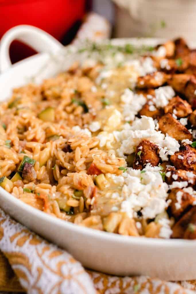 side view of a white dish with Greek orzo pasta with layers of feta cheese and marinated chicken 