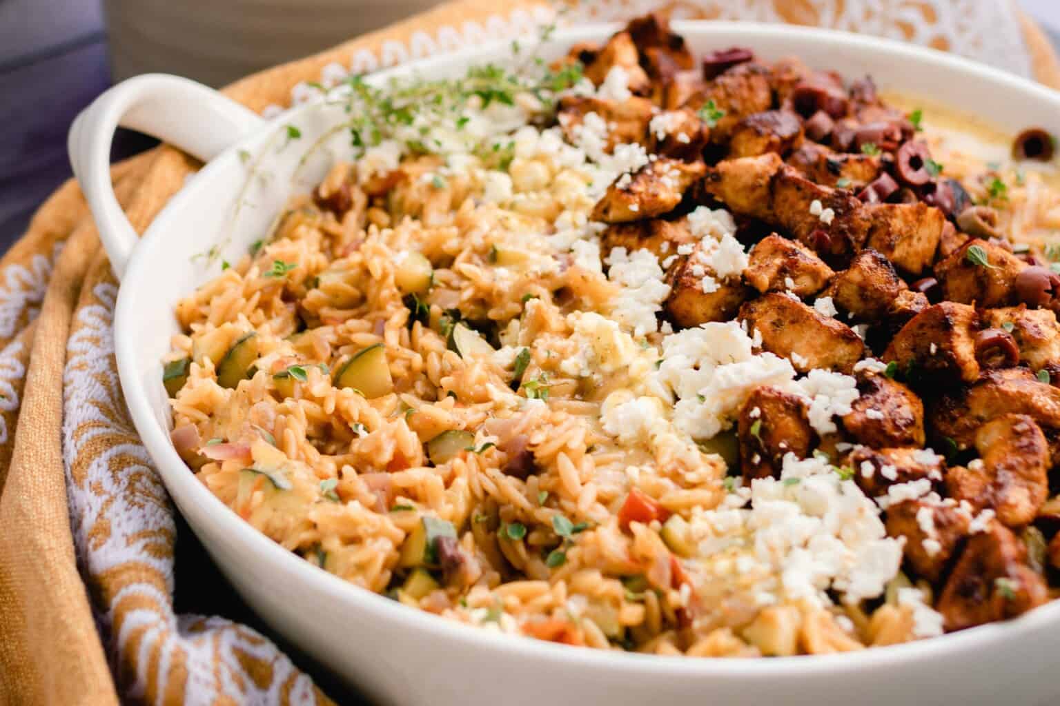 side view of a white dish with Greek orzo with layers of feta, chicken, and olives.