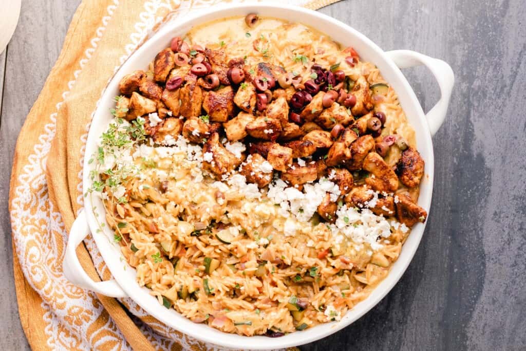 overhead photo of greek chicken with orzo pasta and feta cheese in a white enameled pan on a gray countertop