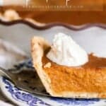 slice of pumpkin pie made from scratch with a dollop of whipped cream on a antique blue and white plate. The rest of the pie is in the background