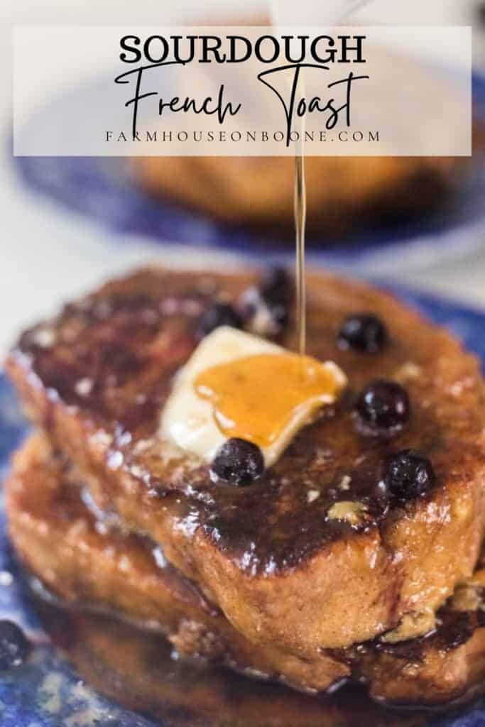 syrup being drizzled over two pieces of sourdough French toast topped with blueberries and butter on a blue plate