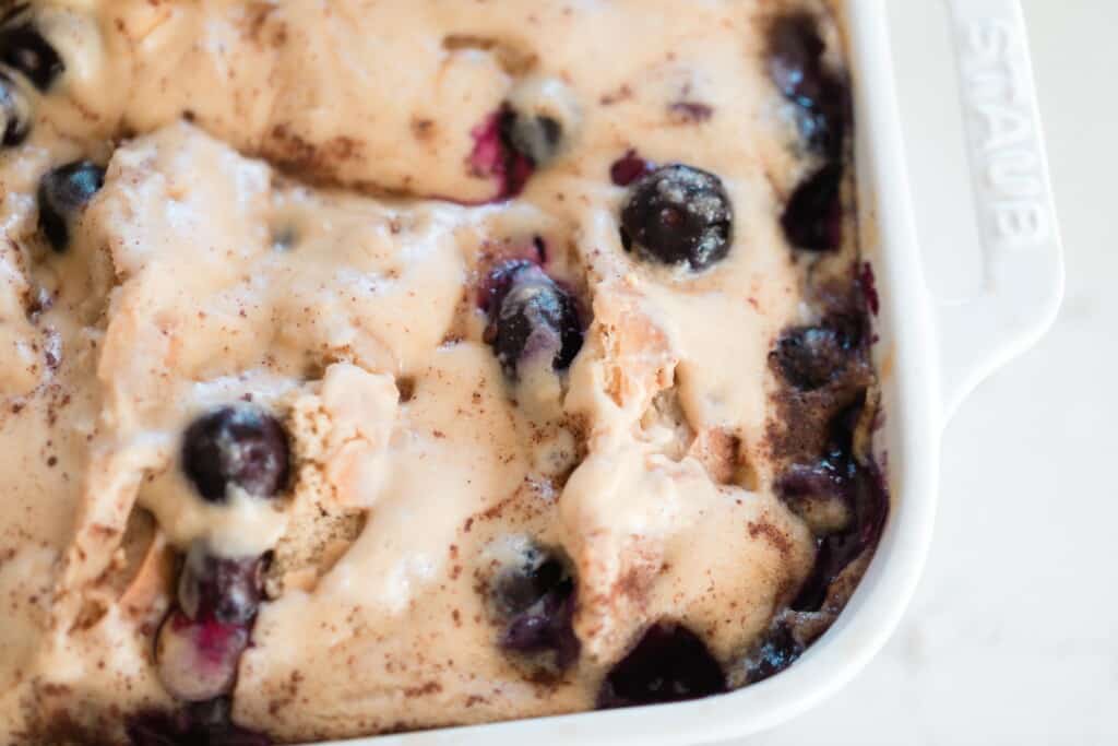 overhead close up picture of stuffed sourdough French toast casserole with blueberries in a white baking dish