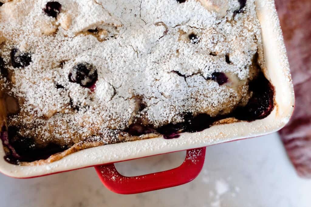 overhead photo of half of a baking dish with stuffed French toast casserole with blueberries and dusted with powdered sugar