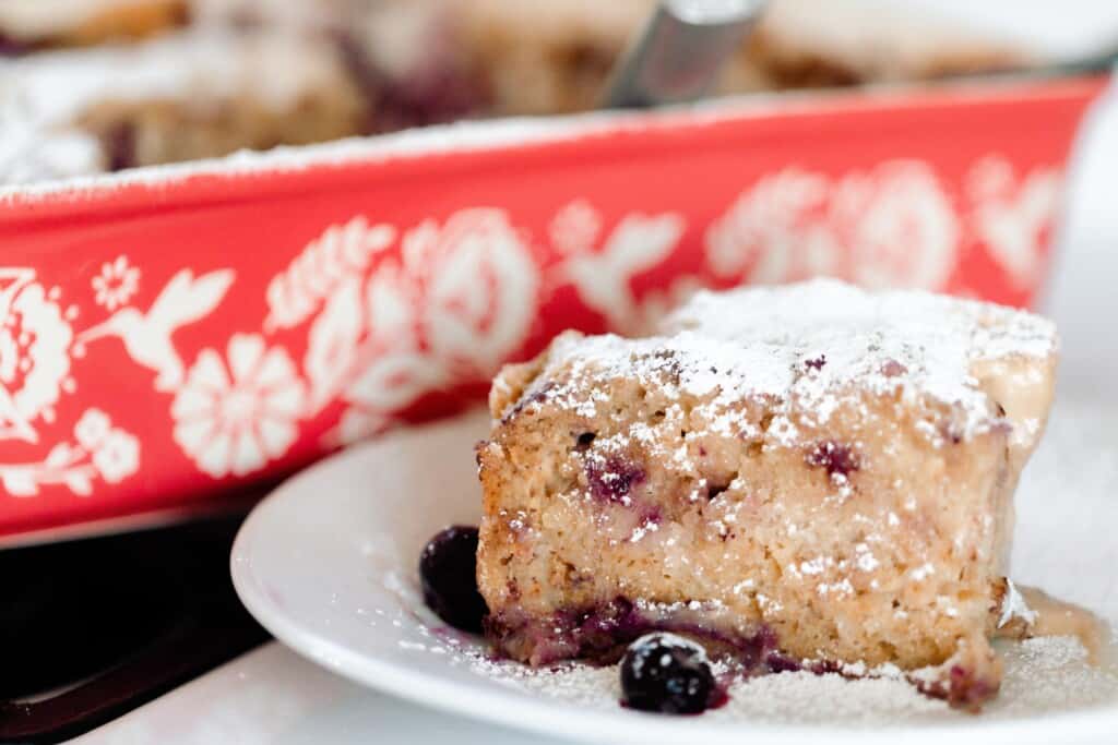 slice of stuffed sourdough French toast casserole on a white plate. A red floral baking dish with more French toast casserole is in the background