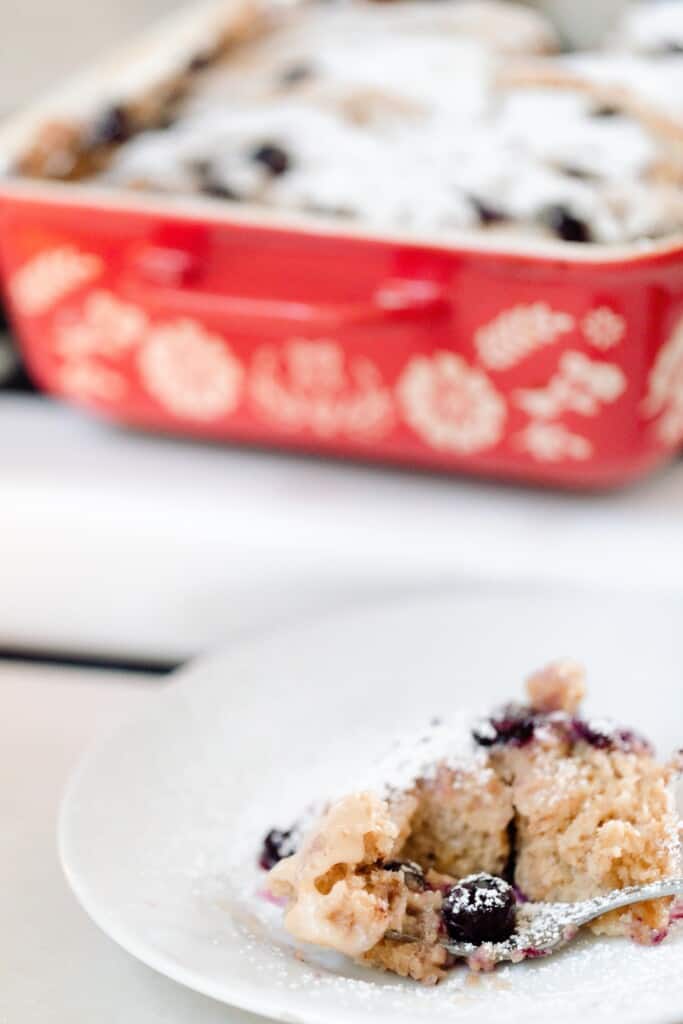 slice of stuffed French toast casserole on a white plate on a countertop wit a red and white floral baking dish on a stove