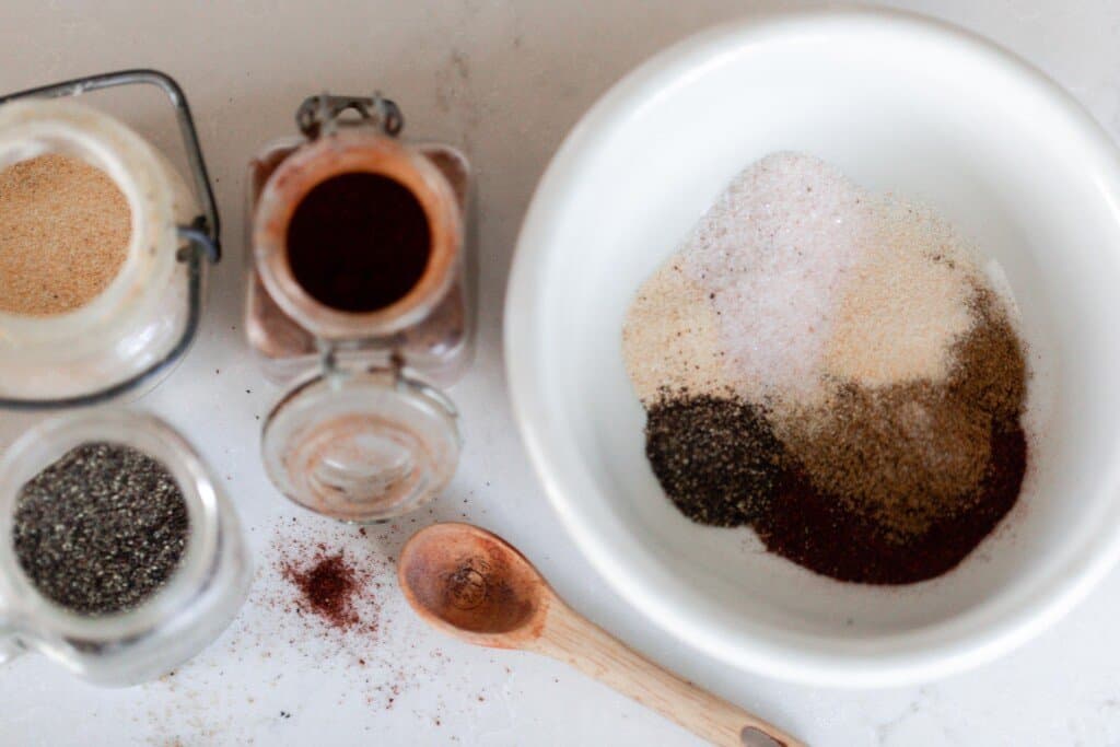 seasonings combined into a white bowl with a wooden spoon sitting on the countertop 