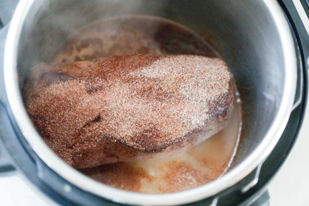 chuck roast seared and sprinkled with seasonings in an Instant Pot With water