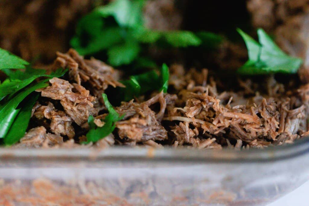 beef carnitas shredded in a glass backing dish topped with cilantro
