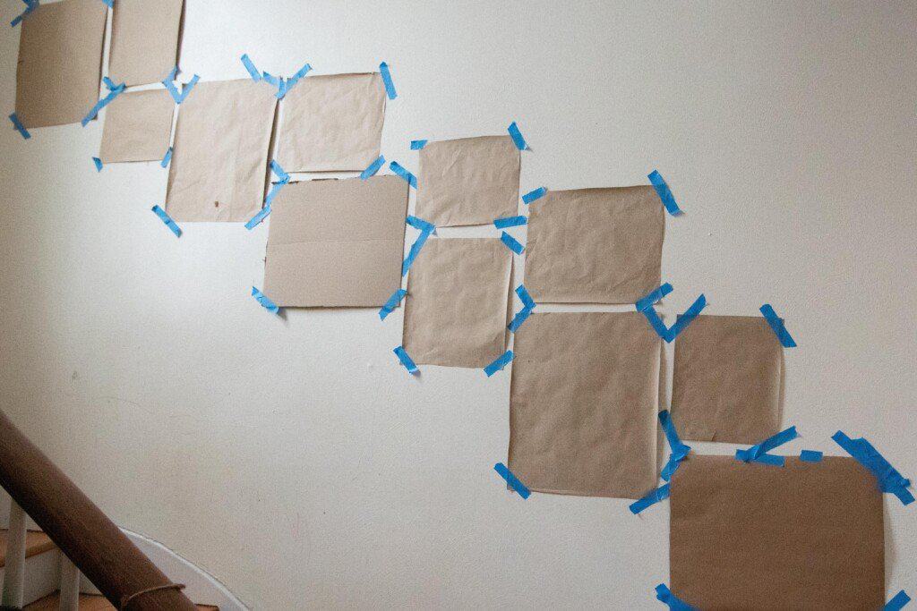 templates of picture frames cut from brown paper taped up on a wall using painters tape to create a gallery wall on a staircase