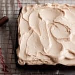 overhead photo of a einkorn gingerbread cake topped with mocha frosting on a wire baking rack on top of a red and white towel