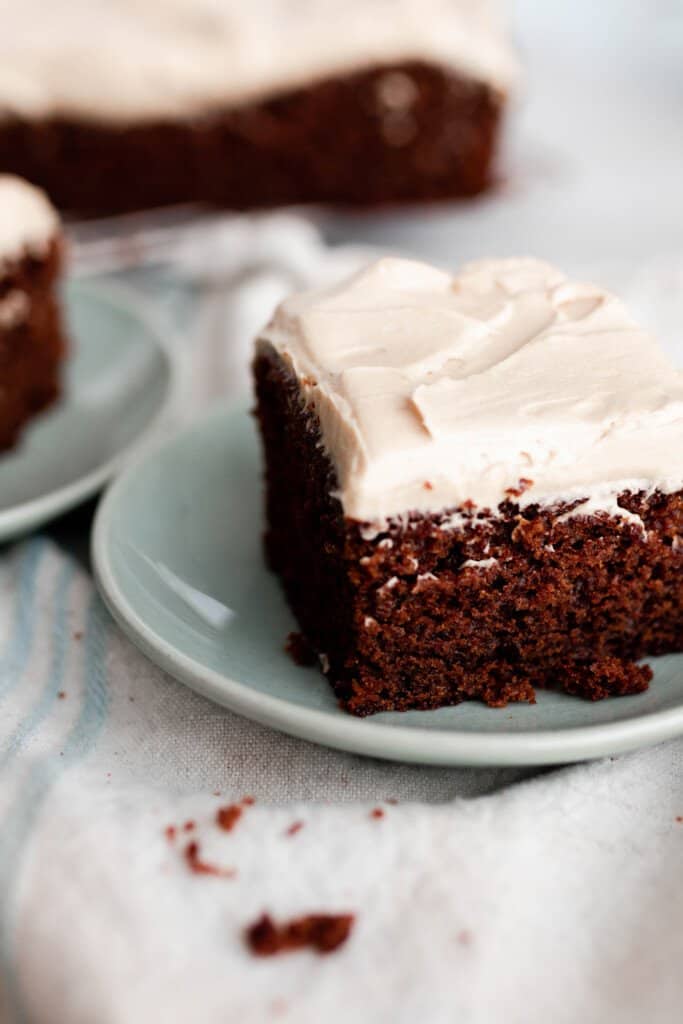 square slices of einkorn gingerbread cake topped with mocha frosting on light teal plates on a white countertop