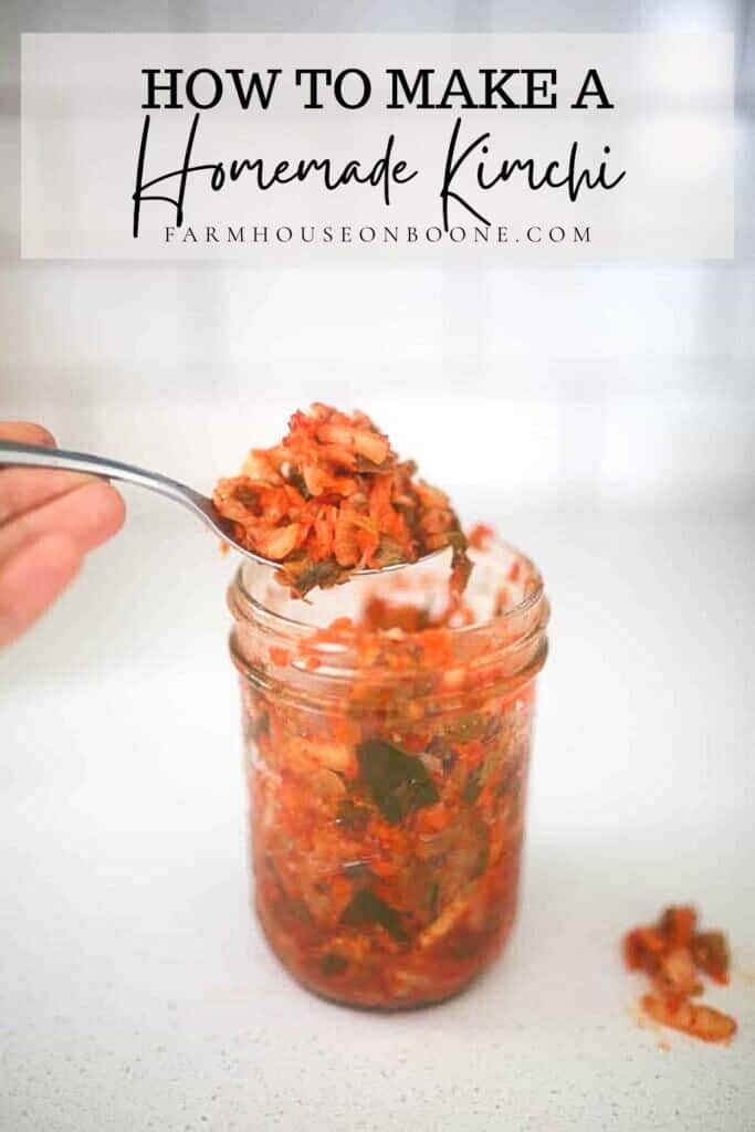 hand holding a spoon of homemade kimchi over a glass pint mason jar of kimchi on a white quartz countertop.