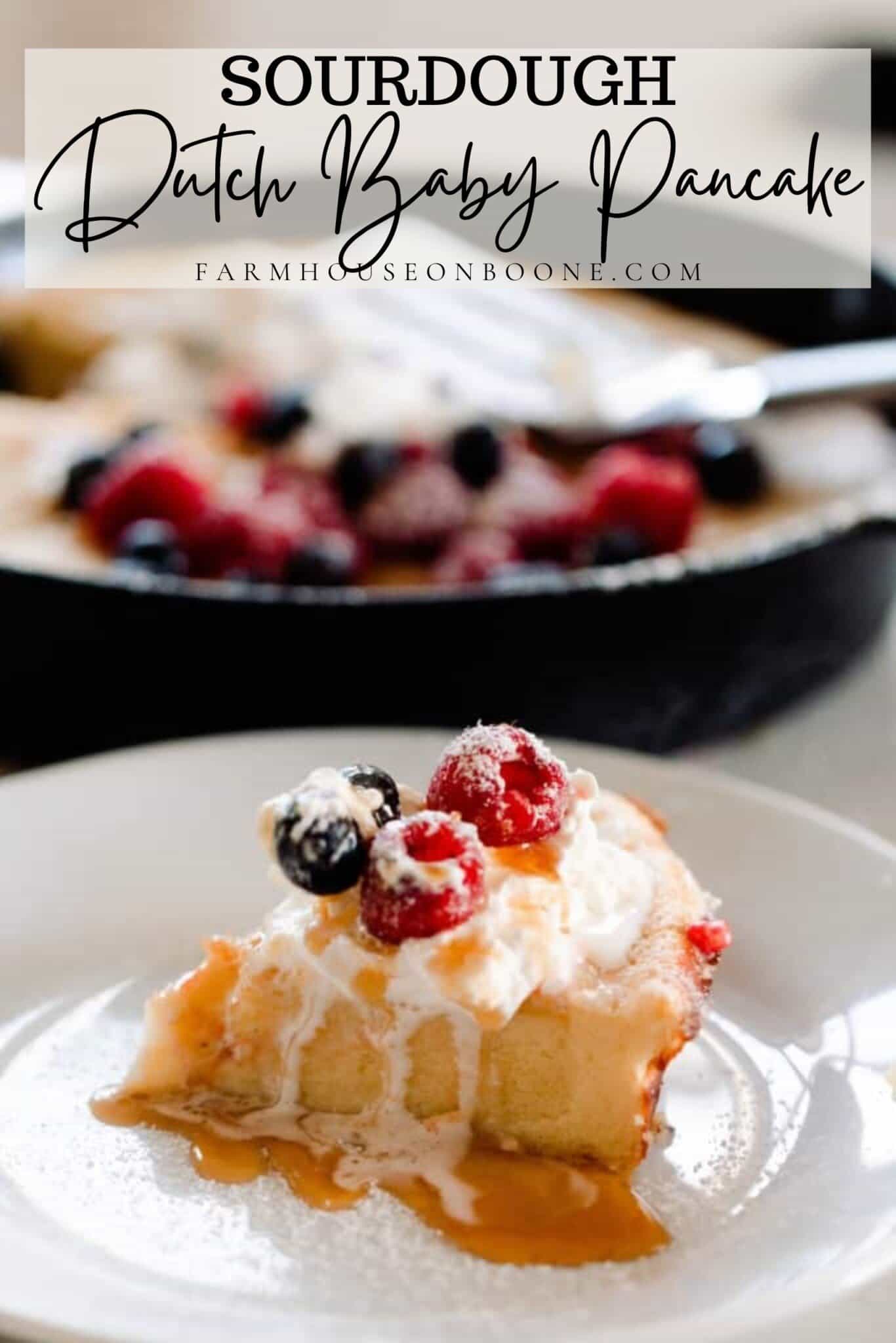 slice of sourdough dutch baby pancake topped with maple syrup, cream, and berries on a white plate with a cast iron skillet with more pancakes in the background