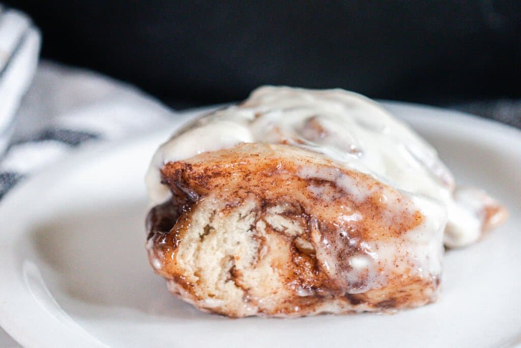 close up side view picture of sourdough cinnamon buns topped with a cream cheese icing on a white plate