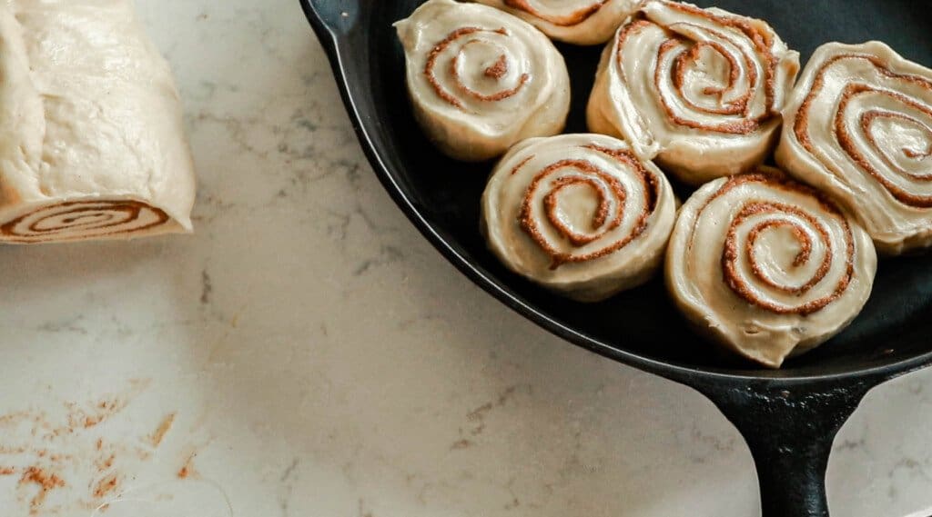 sliced cinnamon rolls being placed onto a cast iron skillet that is on a white quartz countertop