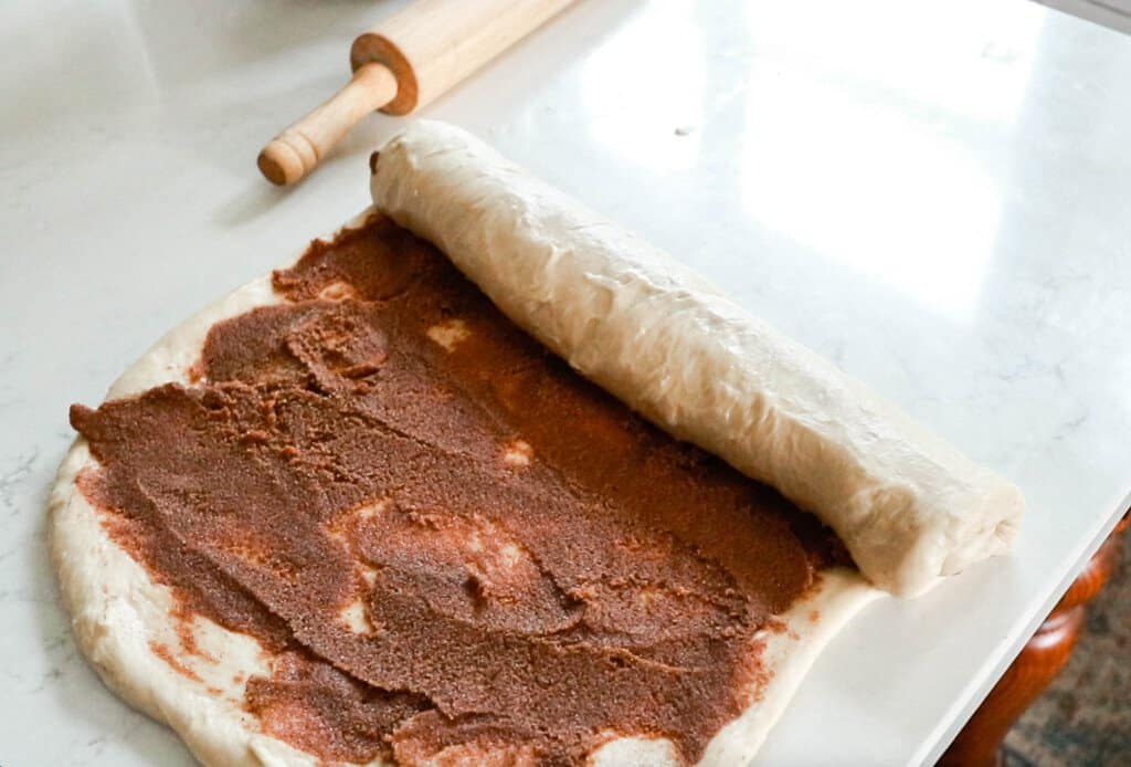sourdough cinnamon rolls are being rolled up into a long roll on a white quartz countertop