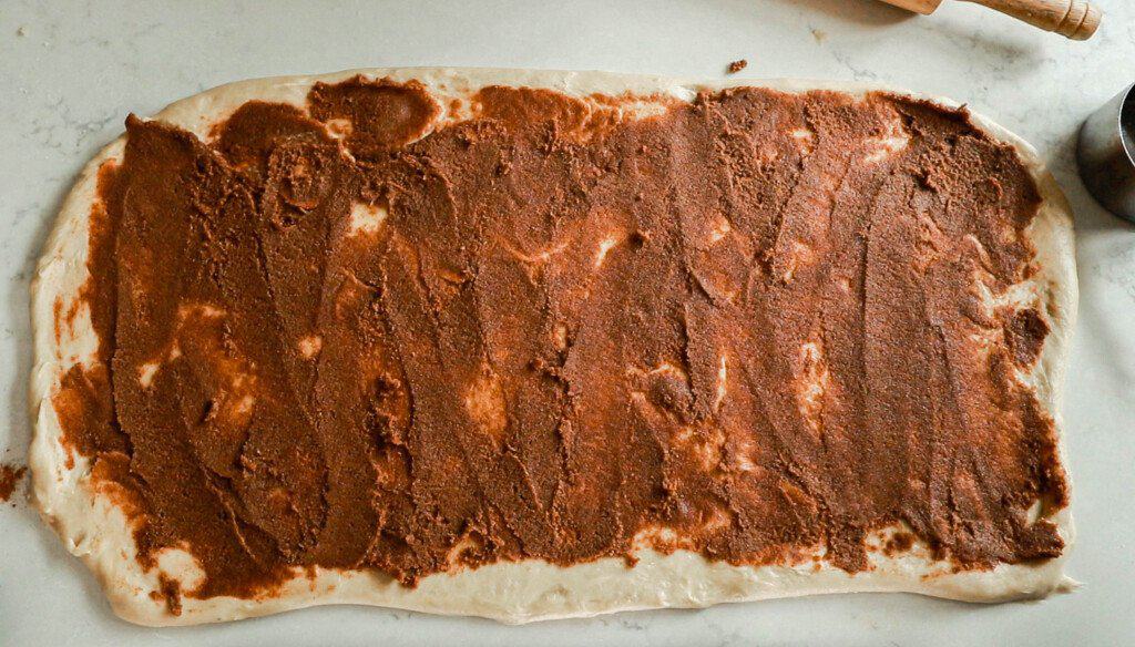 cinnamon roll dough rolled out into a rectangle with butter, cinnamon, and sugar mixture spread evenly on the dough.